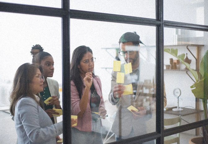 A change management workshop around a wall of sticky notes